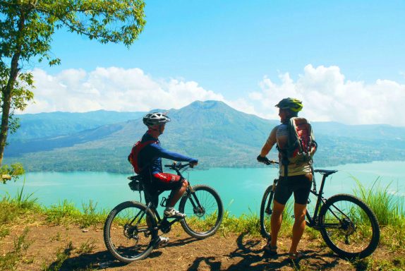 Blick auf den Vulkan Batur Zwei Radfahrer blicken auf einen See und Berge bei schönem Wetter.