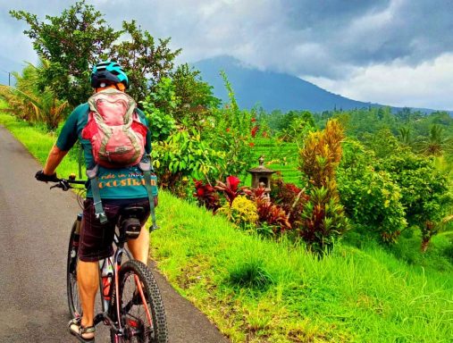 Radtour bei den Reisterrassen Jatiluwih Radfahrer auf einer malerischen Straße mit üppiger Vegetation und einem Berg im Hintergrund.